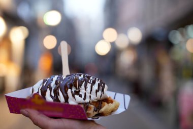 Canlı bir sokak ortamında, üzerinde çırpılmış krema ve çikolata sosu olan yeni servis edilmiş Belçika waffle 'ının yakın çekimi..