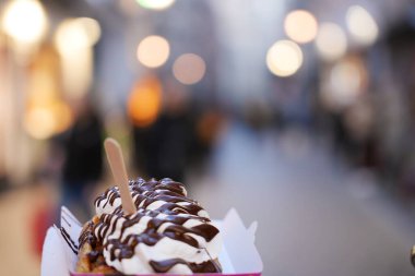 Krem şanti ve çikolata sosuyla kaplı Belçika waffle 'ının yakın çekimi, Brüksel' de canlı bir caddede, bulanık ışık altında tutuluyor..