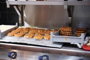 Düzinelerce altın Belçika waffle 'ı tepsilerde ve fırın tezgahının arkasındaki soğutma raflarında dinleniyor..