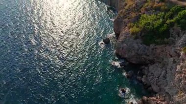 İnsansız hava aracı kıyı kenti siluetini, engebeli uçurumları ve güneş uzak bir sıradağların ardında batarken parıldayan denizi ortaya çıkarmak için yükseliyor..