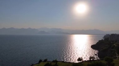 İnsansız hava aracı kıyı şehri üzerinde ilerler, sakin denizi yansıtan güneş ışığını yakalar ve ufukta kaybolan uzak dağları yakalar..