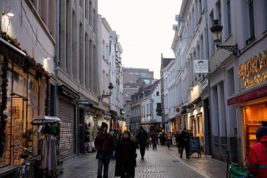 Bruxelles, Belçika 04.01.2025 İnsanlar tarihi bir Avrupa şehrinde butikler, çikolata dükkanları ve bayram mağazalarıyla dolu dar bir kaldırım taşı caddesi boyunca yürüyorlar..