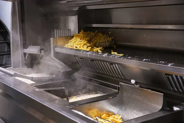 Profesyonel bir kızartma istasyonu faaliyet halinde. Sıcak yağ kaynıyor ve buhar yükseliyor. Patatesler taze pişmiş ve soğuyor.. 