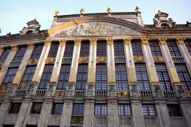 Brüksel 'in Grand Place kentindeki altın barok lonca binasının detaylı manzarası, büyük camlar, oymalar ve dekoratif heykeller yer alıyor.. 