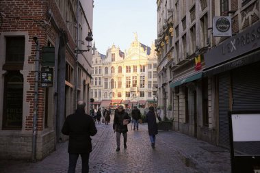 Bruxelles, Belçika 04.01.2025 Brüksel 'de, tarihi binalar ve dükkanlarla çevrili güneşli Grand Place' e doğru yürüyen insanlarla dolu bir cadde..