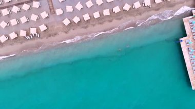 Yüksek perspektiften çekilen turkuaz denizle karşılaşan yumuşak dalgalarla kumlu sahildeki dizilmiş plaj şemsiyelerinin İHA 'dan aşağı görüntüsü. 