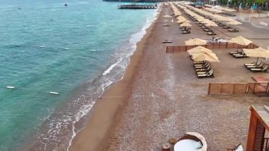 Sakin bir sahil şeridini yavaş bir drone görüntüsü yumuşak dalgalar, kumdaki ayak izleri ve kırsal ahşap bir kulübe. Seyahat, rahatlama ve yaz konseptleri için ideal ortam.. 