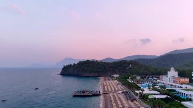 Gün batımında sakin bir sahilin alçak hava manzarası, kumdaki boş güneşlikleri, yumuşak dalgaları ve yumuşak pastel gökyüzünü gösteriyor. Seyahat, rahatlık, sağlık ve romantik kavramlar için idealdir.. 