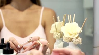 Kadın ellerinin pembe bir gua sha taşı ve yüz silindiri tutarak cilt masajına başlamadan önce onları aynaya yerleştirmeye hazırlandığı yakın plan. 