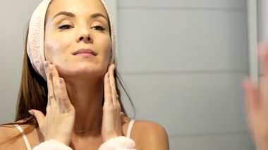 Genç bir kadın ellerini nazikçe boynunda gezdirip aynaya bakarken çene hizası çiziyor. Bu kaldırma masajı onun cilt esnekliğini ve rengini arttırmak için yaptığı ritüelin bir parçası..