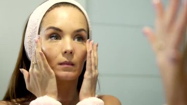 Genç bir kadın aynanın önünde cilt serumu sürerken avuçlarını nazikçe yüzüne bastırıyor. Bu rahatlatıcı kişisel bakım ritüeli serum emilimini arttırır ve parlayan, sağlıklı bir cildi teşvik eder..