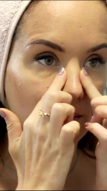 Genç bir kadının, günlük cilt bakımı ve güzellik ritüelinin bir parçası olarak parmaklarıyla gözünün altındaki bölgeye masaj yapması.