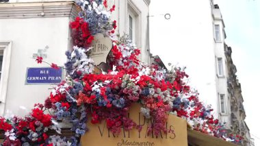 Montmartre Paris 'teki bir dükkanın dış cephesini kaplayan renkli yapay çiçekler, görünür sokak tabelaları ve klasik bina ayrıntılarıyla. Sadece editörler kullanır. Paris, Fransa 04.01.2025 