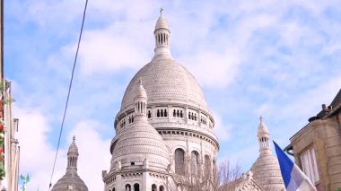 Montmartre 'daki Sacre Coeur Bazilikası' nın ön planda Fransız bayrağı ve dekoratif sokak unsurlarıyla manzarası. Güneşli bir günde açık mavi gökyüzü ile yakalandılar. Editör Paris, Fransa 04.01.2025 