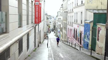 Paris, Fransa 04.01.2025 Adam Montmartre Paris 'te ıslak bir kaldırım taşı caddesinde koşu yapıyor. Şehir binaları, sokak işaretleri ve son yağmurun yansımaları var. Sadece editör kullanımı