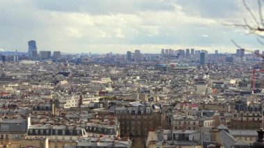 Paris 'in yüksek çatıları, yoğun tarihi binalar ve bulutlu bir gökyüzünün altındaki uzak gökdelenler. Şehir manzarası klasik ve modern mimariyi harmanlıyor.