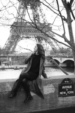 Soğuk bulutlu bir günde Paris 'te New York Bulvarı' nda Eyfel Kulesi 'nin yanında duran gri paltolu şık bir kadın.