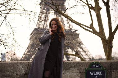 Paris 'te New York Bulvarı' nda Eyfel Kulesi 'nin yanında duran gri ceketli bir kadının görüntüsü. Kış ağaçları ve arka planda Seine nehri var. 