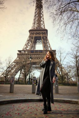 Paris 'te bir kaldırım taşı caddesinde Eyfel Kulesi' nin yanında poz veren şık giyinmiş kendine güvenen genç bir kadın.. 