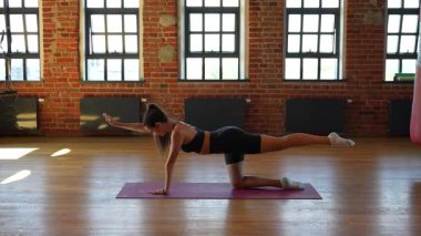 Atletik kadın paspas üzerinde kuş köpek yogası yapıyor. Kolları ve bacakları esnek. İç mekan fitness ve sağlıklı yaşam süresince dengelerini koruyor.