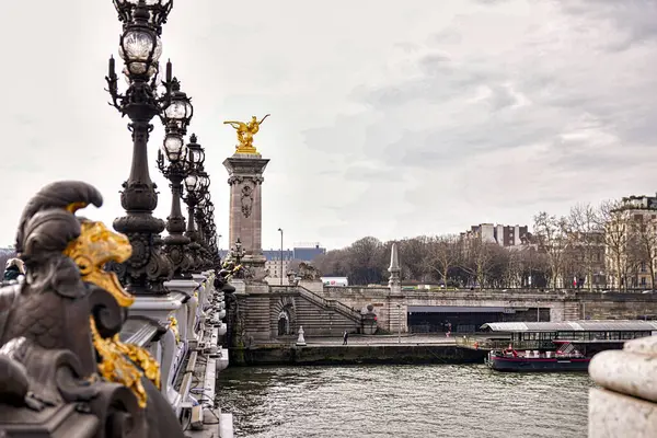 Paris 'teki tarihi Alexander Köprüsü' ndeki dekoratif elementlerin ve fenerlerin kapatılması bulutlu gökyüzünün altında nehir ve şehir arkaplanı. 