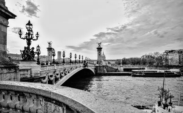 Paris 'teki Alexander Köprüsü' nün klasik monokrom fotoğrafı. Heykel fenerleri, taş korkuluklar ve dramatik gökyüzü altında nehir manzarası..