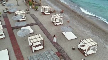 Sahildeki bir tatil beldesinde çıplak ayakla dans eden bir kadının çıplak ayakla sahile yakın bir yerde şemsiyesi ve kabinesi olan bir kadının görüntüsü. Gökyüzünden sakin bir yaz ortamında yakalanmış.