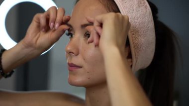 Evde yüz bakımı rutini sırasında alnını rahatlatmak ve kaldırmak için kaş bölgesine masaj yapan bir kadının yakından görünüşü.