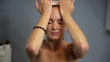 Kadın, yüz masajının son aşamasında avuçlarını alnında gezdirir. Kendine dikkat etmeyi ve sakin bir ev ortamında yüz kaslarını gevşetir.