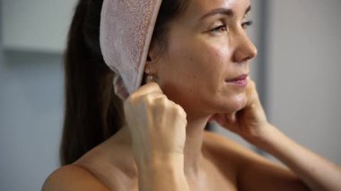 Parmak eklemleriyle boyun ve çene masajı yapan, pembe bir saç bandı ve çıplak omuzlar takan bir kadının yakın görüntüsü.