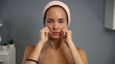 Kadın, yüz masajı sırasında eklemleriyle burun kıvrımlarının yakınına baskı uyguluyor. Ev ortamında pembe bir saç bandı takıyor.