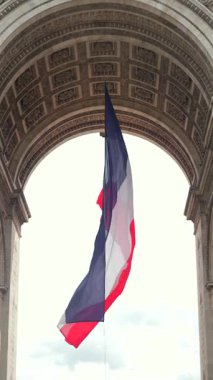 Fransa 'nın başkenti Paris' teki Zafer Takı 'nın altında asılı arka ışıklandırılmış Fransız üç renkli bayrağı. Parlak gökyüzü ve mimari tavan detayları yukarıda görünüyor..