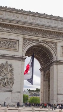 Fransa 'nın başkenti Paris' teki Zafer Takı 'nın altında dalgalanan Fransız üç renkli bayrağının görüntüsü, turistler 8 Temmuz 2025' te yakınlarda yürüyorlar..