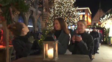 Turistler, 5 Ocak 2024 'te Münih' teki bir Noel pazarında açık havada sıcak içeceklerin keyfini çıkarırken, festival ışıklarına ve dekorasyonlarına hayranlık duyuyorlar.