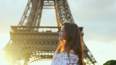 Gülümseyen genç kadın Eyfel Kulesi 'nin önünde altın saatinde poz veriyor. Saçları akşam güneşinde parlıyor.
