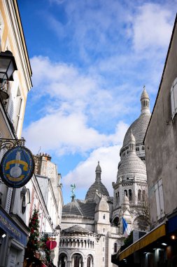 Montmartre caddesinde yükselen Sacre Coeur Bazilikası 'nın dikey görüntüsü Paris, Fransa' da bayraklar ve dükkanlar. 22 Şubat 2025 'te yakalandı..