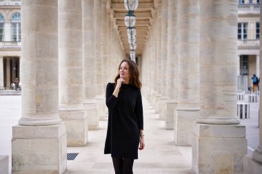 Siyah elbiseli çekici bir kadın Paris, Fransa 'da Palais Royal' in klasik taş sütunları arasında düşünceli poz veriyor..