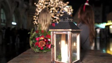 Sıcak, parlayan mum feneri ve şenlikli bir kış akşamında kırsal bir ahşap masada kırmızı süslemeler ve çam dallarıyla dekoratif tatil buketi. 