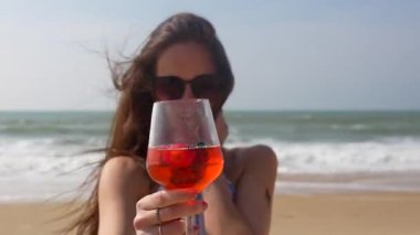 Termoli İtalya plajında elinde bir bardak turuncu kokteyl tutan güneş gözlüğü takan genç bir kadın, 31 Temmuz 2025 'te sadece editoryal kullanım