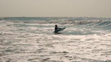 Güneşli bir günde okyanus dalgalarında sörf tahtasında oturan sörfçü.