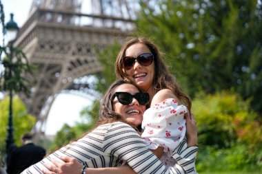Neşeli bayan arkadaşlar güneşli Paris 'te Eyfel Kulesi' nin yakınında kucaklaşıyorlar.