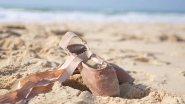 Balerin ayakkabıları deniz kenarında yumuşak kumda dinleniyor ve doğal ışıkta kurdeleler takıyor. 