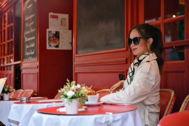 Trençkotlu şık bayan şık Paris kafesinde kahve ile oturuyor.