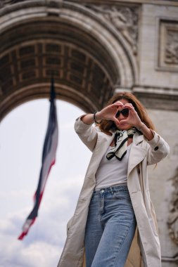 Paris 'te gülümseyen bir kadın kalp şekli oluşturuyor. Elleri Zafer Takı' nın önünde ve Fransız bayrağı sallıyor. 