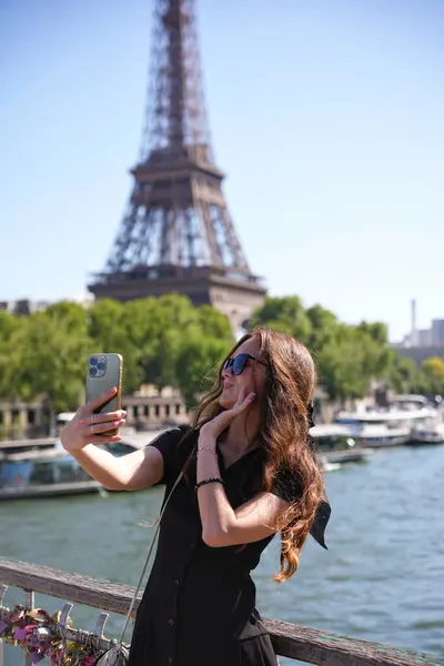 Paris 'te güneşli bir günde Eiffel Kulesi yakınlarında akıllı telefonuyla selfie çeken bir kadın.