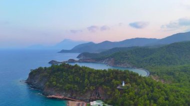 Bereketli orman tepeleri ve pastel gökyüzünün altındaki katmanlı dağlarla dolu huzurlu gizli körfezin havadan görünüşü.