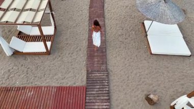 Yazlık elbiseli bir kadın Tahta sahil yolunda yürüyor