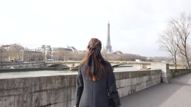 Paris 'teki Seine Nehri' nde yürüyen bir kadın Eyfel Kulesi 'nin arka planında Fransa