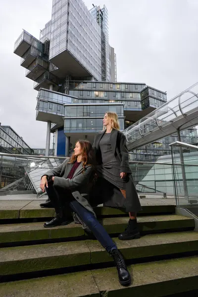 Arka planda modern cam bina ile basamaklarda poz veren moda kadınları