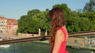 Kırmızı yaz elbiseli, güneş gözlüklü turist Venedik Kanalı 'nın yanında duruyor.